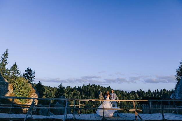 Após o casamento, um casal alegre dança na ponte contra o pano de fundo de belas montanhas e floresta verde