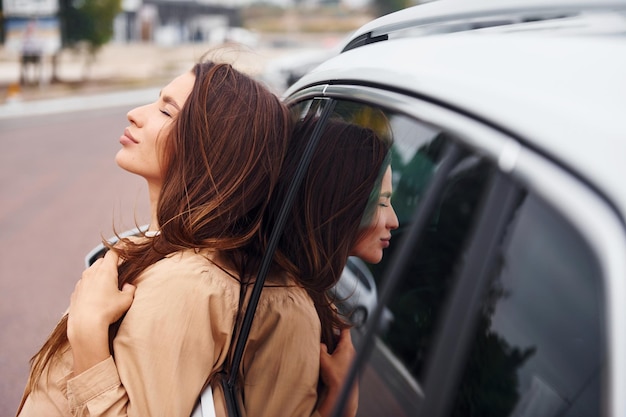 Se apoya en la puerta Hermosa mujer joven de moda y su automóvil moderno