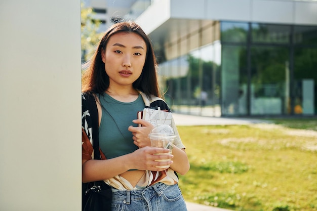 Apoyado en la pared, la mujer asiática joven está al aire libre durante el día