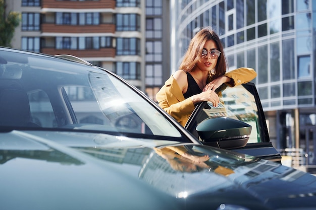 Apoyado en la puerta Joven mujer de moda con abrigo de color burdeos durante el día con su coche