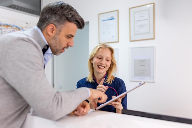 Apoyando a los pacientes Hombre sonriente y su alegre dentista juntos llenando un formulario en la recepción