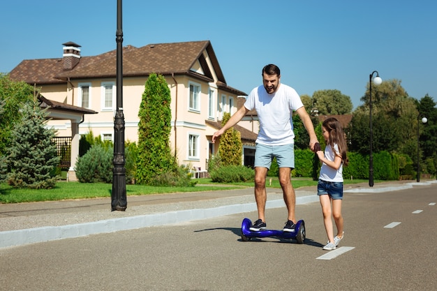 Apoyándote. niña linda que sostiene la mano de su amado padre montando en un hoverboard por la calle y brindándole apoyo