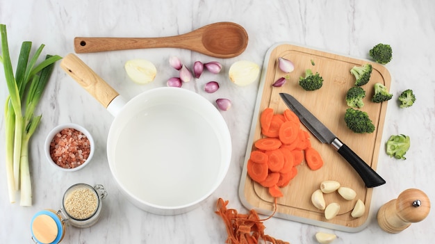 Apoyos de la comida Cacerola de cerámica blanca vacía con ingredientes vegetales alrededor. Espacio en blanco para texto o publicidad. Preparar vegetales salteados con brócoli y zanahoria para cocinar