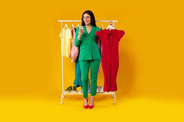 App für Online-Shopping Junge europäische Dame mit Handy und Kleid, die Kleidung online in der mobilen App bestellt