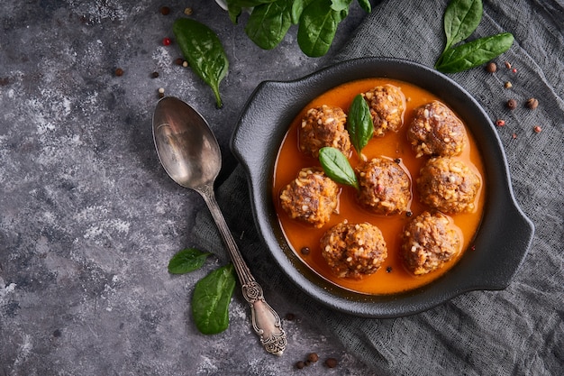 Appetitanregende selbst gemachte Fleischklöschen mit Tomatensauce und Spinat dienten in einer Platte auf einer dunklen Steintischplatteansicht