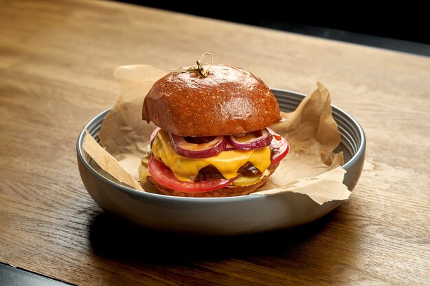 Appetitanregender Cheeseburger mit Zwiebeln und Tomaten in einem Teller auf einem hölzernen Hintergrund