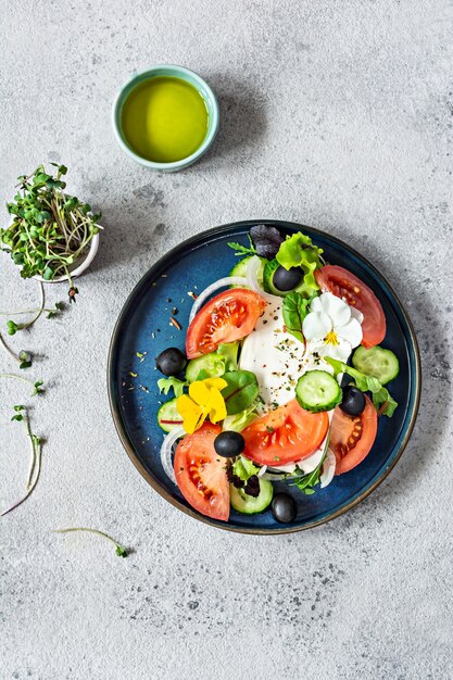 Appetitanregender Salat mit Feta-Käse frisches Gemüse Tomaten Gurken Zwiebeln knuspriger Salat Microgreens und violette Blüten Außergewöhnliche Portion griechischer Salat Essen mit Blumen