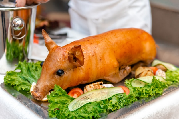 Appetitanregendes gebratenes Spanferkel auf einem hölzernen Behälter mit Zitrone und Grüns