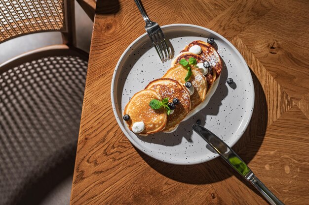 Appetitlich leckere Pfannkuchen auf einem weißen Teller mit Ahornsirup Blaubeeren und Minze auf einem schönen Holztisch Das Restaurant serviert Ihre hausgemachten Lieblingsgerichte