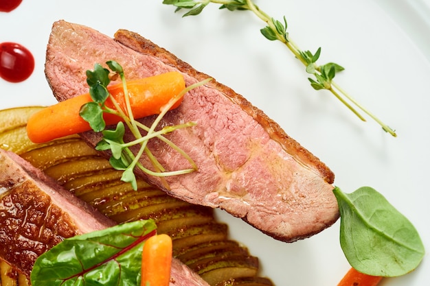 Appetitliche Confit-Entenbrust mit Birnen- und gelbem Apfelpüree, Beerensauce in einem weißen Teller. Auf grauer Oberfläche isoliert.