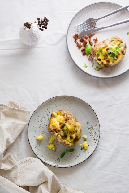Appetitliche, doppelt gebackene Kartoffeln in ihren Schalen mit Käse- und Speckkrümeln auf Tellern auf einem Holztisch Flexitarian Diet Top und vertikale Ansicht