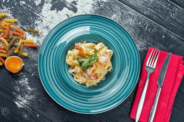 Appetitliche hausgemachte Pasta mit Garnelen und cremiger Sauce in einem blauen Teller. Nahaufnahme, Draufsicht. Italienische Spaghetti, Foto für das Rezept