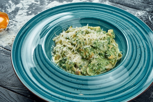 Appetitliche hausgemachte Pasta mit Spinatsauce und Lachs in einem blauen Teller. Nahaufnahme, Draufsicht. Italienische Spaghetti, Foto für das Rezept