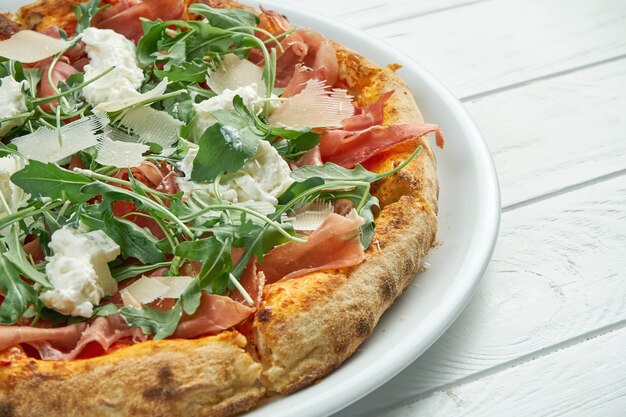 Appetitliche hausgemachte Pizza mit Jamon, Parmesan, Rucola und Straccella auf einem weißen Teller auf einem weißen