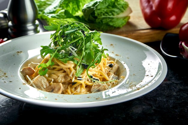 Appetitliche italienische Pasta mit Waldpilzen und weißer Sauce, serviert in einem weißen Teller auf einem dunklen Marmortisch. Italienische Spaghetti. Restaurant Essen