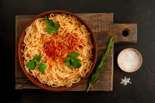 Appetitliche italienische Pasta-Spaghetti mit Tomatensauce, Parmesan auf einem Teller, Schneidebrett auf einem konkreten Hintergrund. Sicht von oben