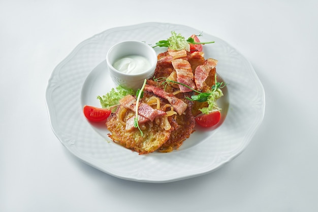 Appetitliche Kartoffelpuffer (Deruny) mit Speck und Sauerrahm in einem weißen Teller auf einem weißen Teller. Ukrainisches Essen