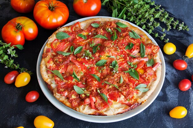 Appetitliche Pizza mit Tomaten auf einer dunklen Oberfläche