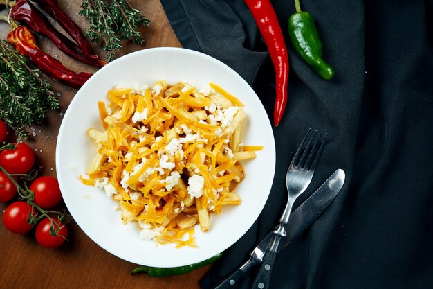 Appetitliche Pommes Frites mit Cheddar-Käse in einer weißen Schüssel auf einem Holztisch in einer Zusammensetzung mit Zutaten. Pommes Frites mit Belag