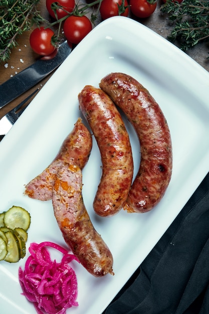 Appetitliche saftige Schweinehackwurst, gebacken in einem Raucher mit Cheddar in einem weißen Teller mit Gemüsekonserven. Deutscher Biersnack