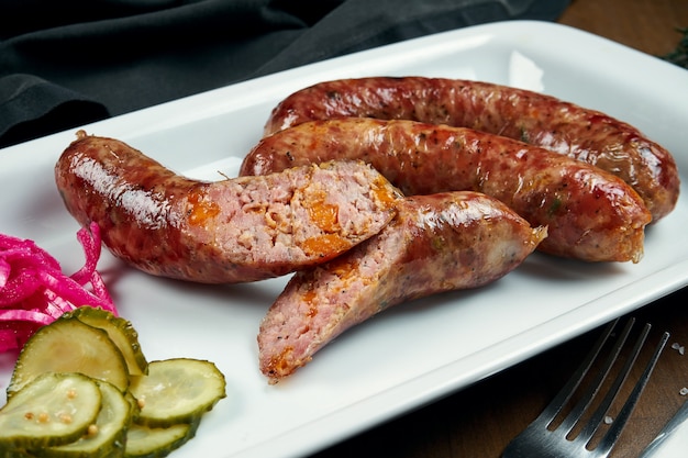 Appetitliche saftige Schweinehackwurst, gegrillt in einem Raucher mit Cheddar in einem weißen Teller mit Gemüsekonserven. Deutscher Biersnack