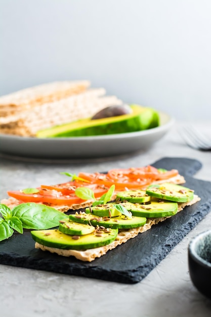 Appetitliche Sandwiches mit Avocado und Tomaten auf Körnerbrot auf Schiefer auf dem Tisch Vegetarische gesunde Ernährung Vertikale Ansicht Selektiver Fokus