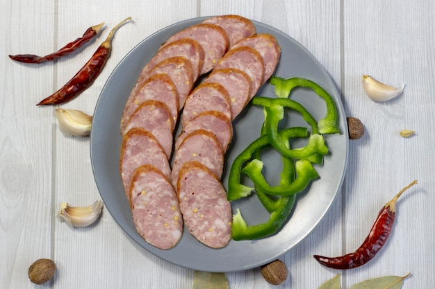 Appetitliche Wurst, geschnitten auf einem grauen Teller auf hellem Holzhintergrund mit grünem Paprika-Chili aus nächster Nähe