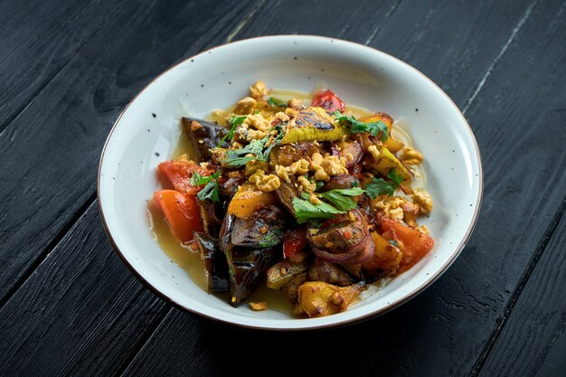 Appetitlicher, diätetischer Salat aus gebackenem Gemüse (Tomaten, Paprika, Auberginen) mit Sauce und Nüssen in einem weißen Teller