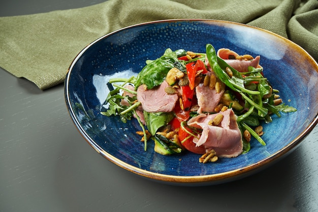 Appetitlicher warmer Salat mit Kalbsgrill und Gemüse, Spinat und Pinienkernen in einer blauen Schüssel auf Holztisch. Gesundes Essen. Nahaufnahme, Speicherplatz kopieren