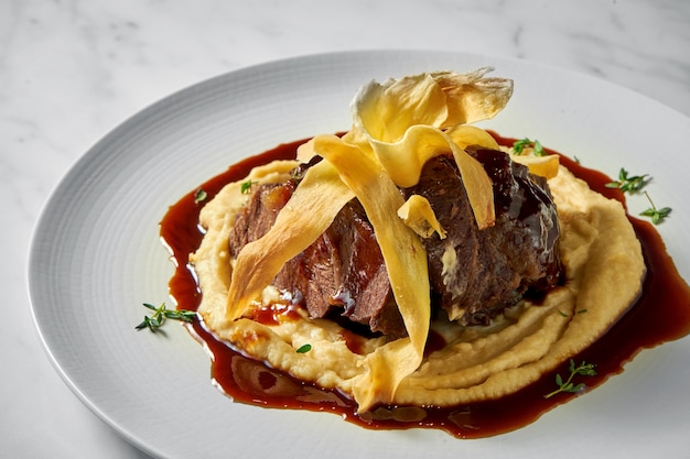 Appetitliches Büffelbackensteak, garniert mit Kartoffelpüree und roter Sauce, serviert in einem weißen Teller auf Marmor