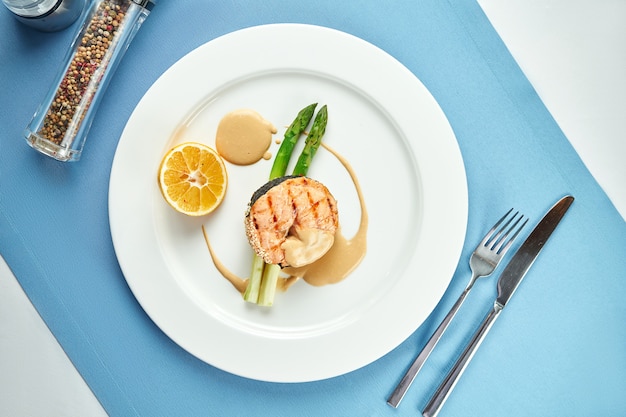 Appetitliches Lachssteak mit Spargel und Sauce in einem weißen Teller auf blauer Tischdecke.