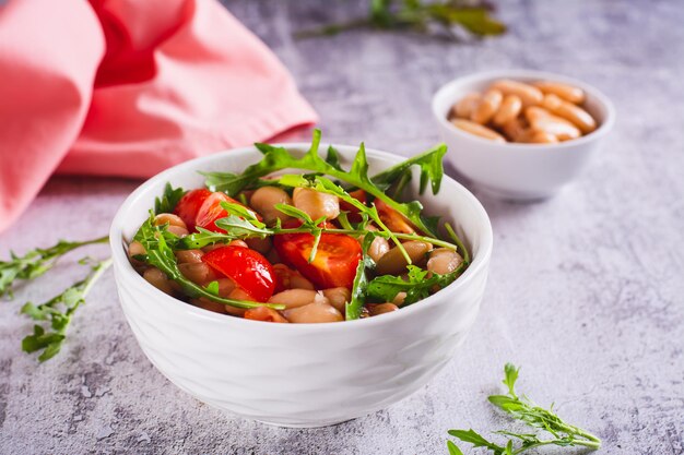 Appetitzender Salat aus Konserven aus weißen Bohnen, Kirschtomaten und Arugula in einer Schüssel