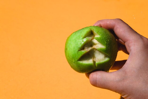 Apple auf einem soliden orangefarbenen Hintergrund in der Hand Weihnachtsbaum in einem Apfel geschnitzt
