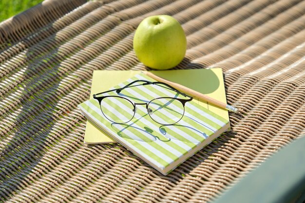 Apple-Buch-Bleistift-Brille-Notizbuch auf Gartenstuhl im Freien. Hinterhof-Studie.