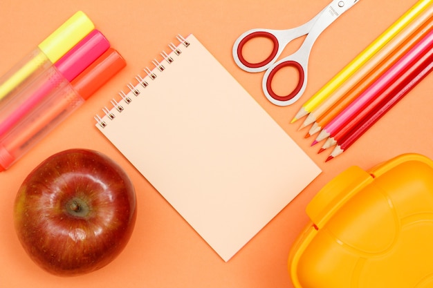 Apple, Filzstifte, Notizbuch, Schere, Farbstifte und Lunchbox auf rosa Hintergrund. Draufsicht mit Kopienraum. Zurück zum Schulkonzept. Schulbedarf. Pastellfarben