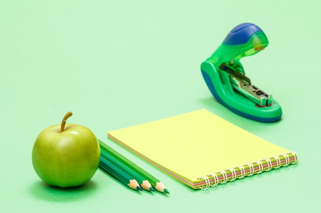 Apple, lápis de cor, caderno e grampeador sobre fundo verde. de volta ao conceito de escola. material escolar. profundidade superficial de campo.