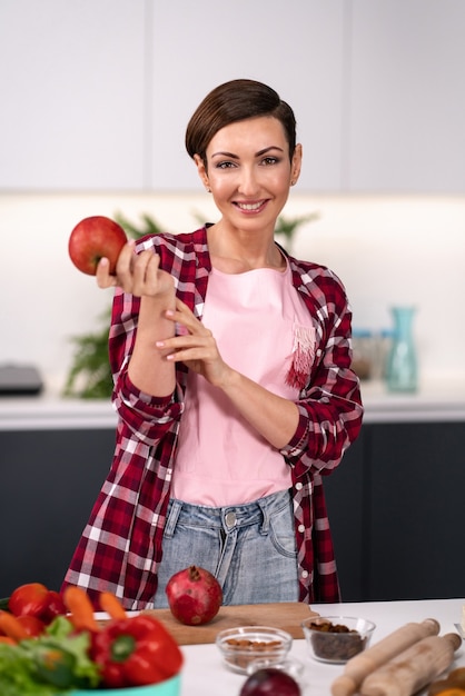 Apple en mano mujer feliz seleccione frutas cocinando en la cocina. Ama de casa cocinando tarta de manzana de pie en la cocina vistiendo camisa a cuadros con un pelo corto