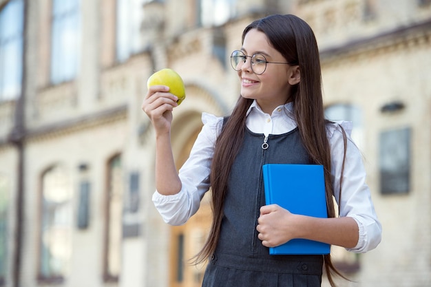 Apple pro Tag hält den Arzt fern. Kleines Kind hält Apfel und Buch im Freien. Apfel-Snack. Snack für die Schule. Gesundes Essen und Ernährung. Biologische und natürliche Ernährung. Gesundheitserziehung. Vitamine richtig einnehmen.