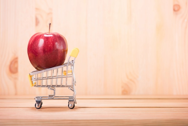 Apple rojo en el carrito de compras con fondo de piso de madera