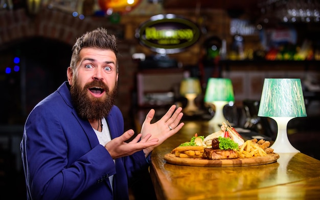 Aprecie a refeição cheat meal concept hipster com fome come comida frita de pub restaurante cliente hipster terno formal sente-se no balcão do bar homem recebeu refeição com batata frita peixe varas carne refeição deliciosa