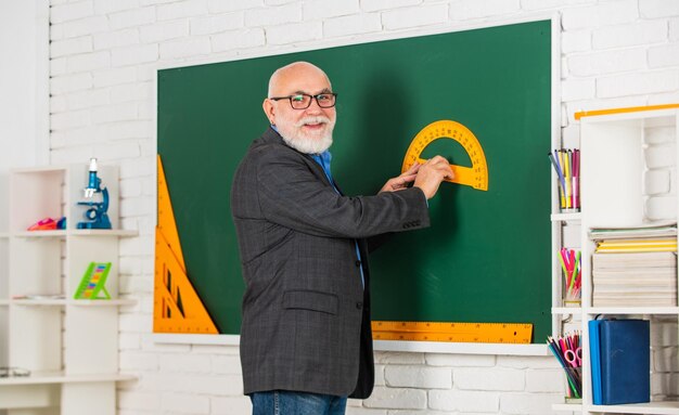 Foto aprenda geometría fácilmente, vuélvase bueno en matemáticas en el salón de clases. el maestro mayor usa la herramienta en la pizarra. tutor barbudo en anteojos. volver a la escuela.