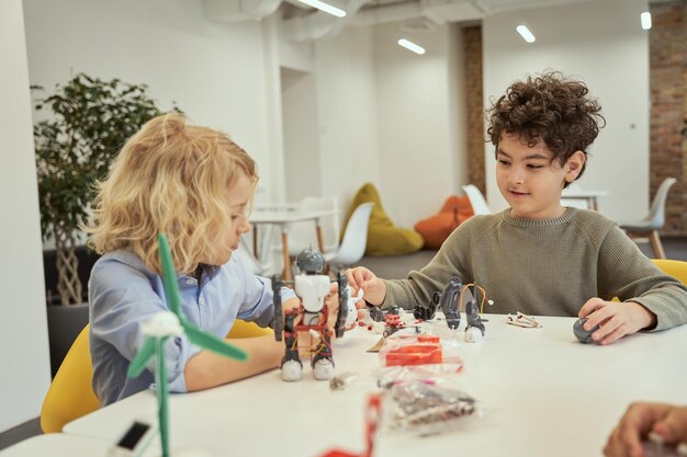 Aprenda de su propia experiencia niños pequeños alegres que examinan y juegan con robots sentados en