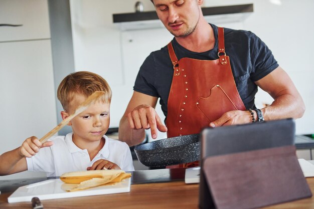 Foto aprendendo a cozinhar pai e filho estão dentro de casa juntos