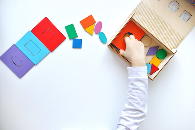 Aprendendo cores e formas. Brinquedo infantil de madeira. A criança coleta um classificador. Brinquedos lógicos educativos para crianças.