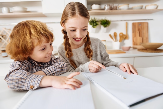 Aprendendo novas coisas. Mulher inteligente e determinada sendo uma tutora para seu irmão enquanto os dois passam um tempo na cozinha e trabalham em suas tarefas de casa