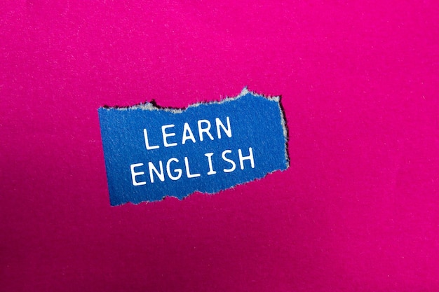 Aprender inglés mensaje escrito en un pedazo de papel azul rasgado en un fondo rosado Símbolo conceptual de aprender inglés Copiar espacio