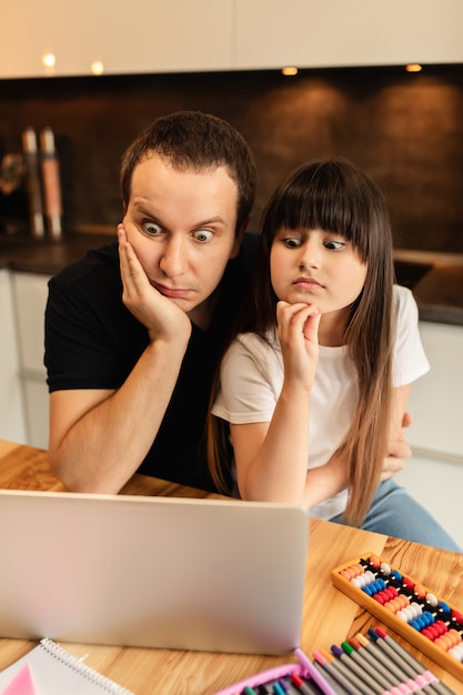 Aprender en línea. la colegiala y su padre miran una lección de video en la computadora portátil en casa. educación a distancia. convivencia familiar