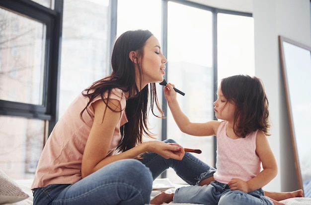 Aprendiendo a maquillar a la joven madre con su hija pasando el fin de semana juntos en la habitación