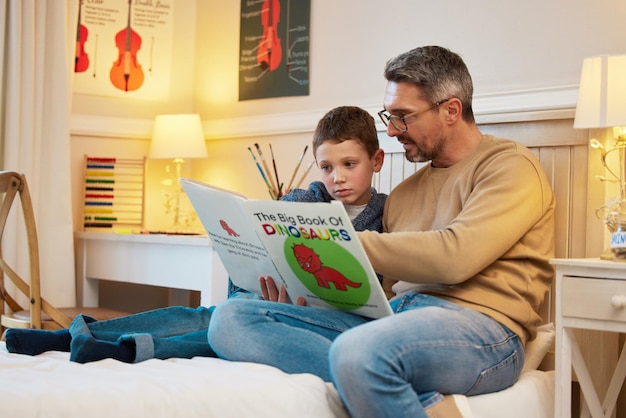 Aprendiendo sobre la historia de estas fascinantes criaturas Fotografía de un padre y su hijo leyendo juntos un libro sobre dinosaurios en un dormitorio de su casa