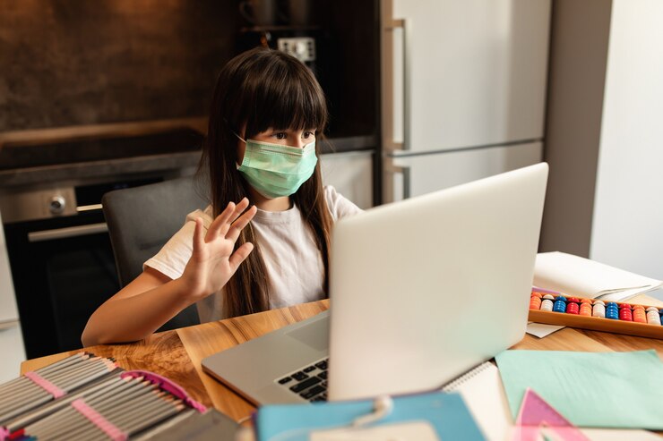 Aprendizado on-line durante a quarentena. Menina com uma máscara protetora no rosto fala com outros participantes na aula de vídeo on-line. Educação on-line em casa.